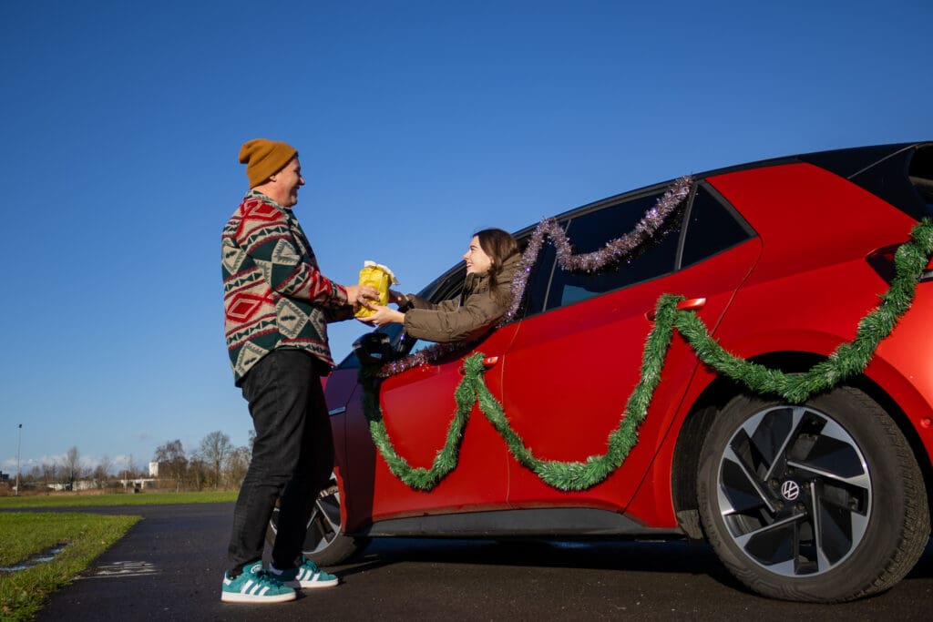 Een persoon die een zak oliebollen geeft aan iemand in een auto tijdens De Oliebollen Drive-in in Breda bij Breepark
