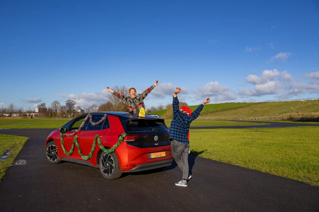 Twee juichende mensen bij auto met oliebollen in de hand tijdens De Oliebollen Drive-in Breda