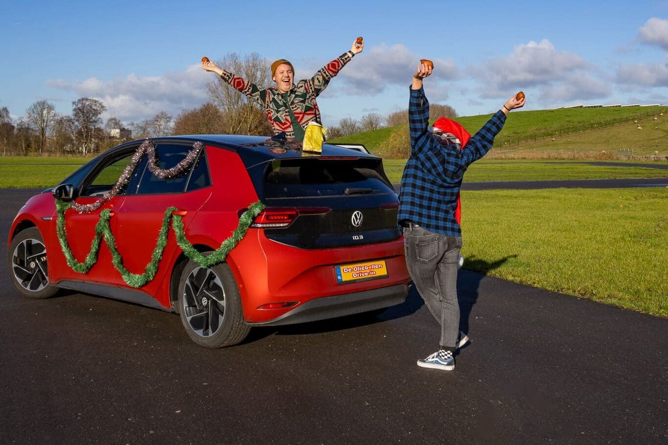 Twee juichende mensen bij auto met oliebollen in de hand tijdens De Oliebollen Drive-in Breda